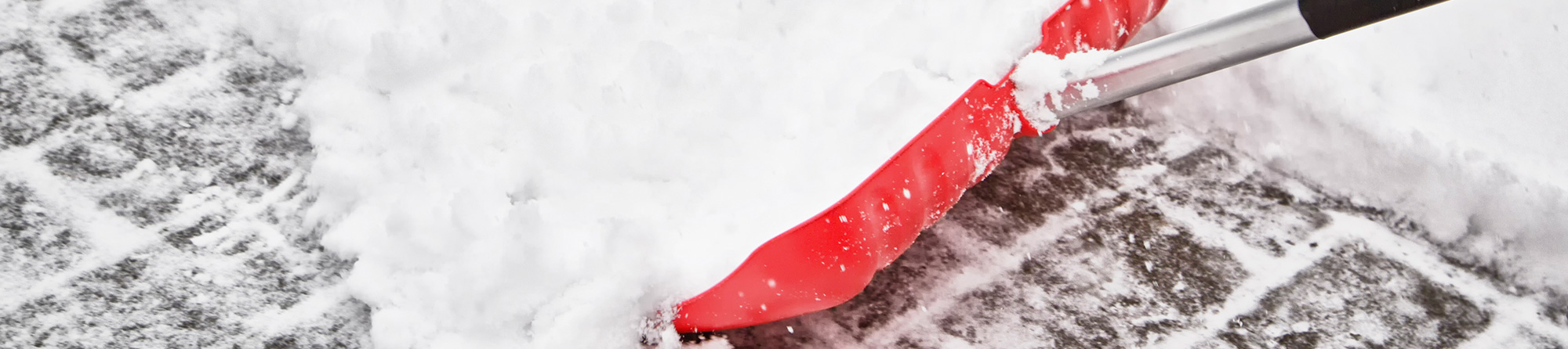 snow shoveling with red shovel on sidewalk