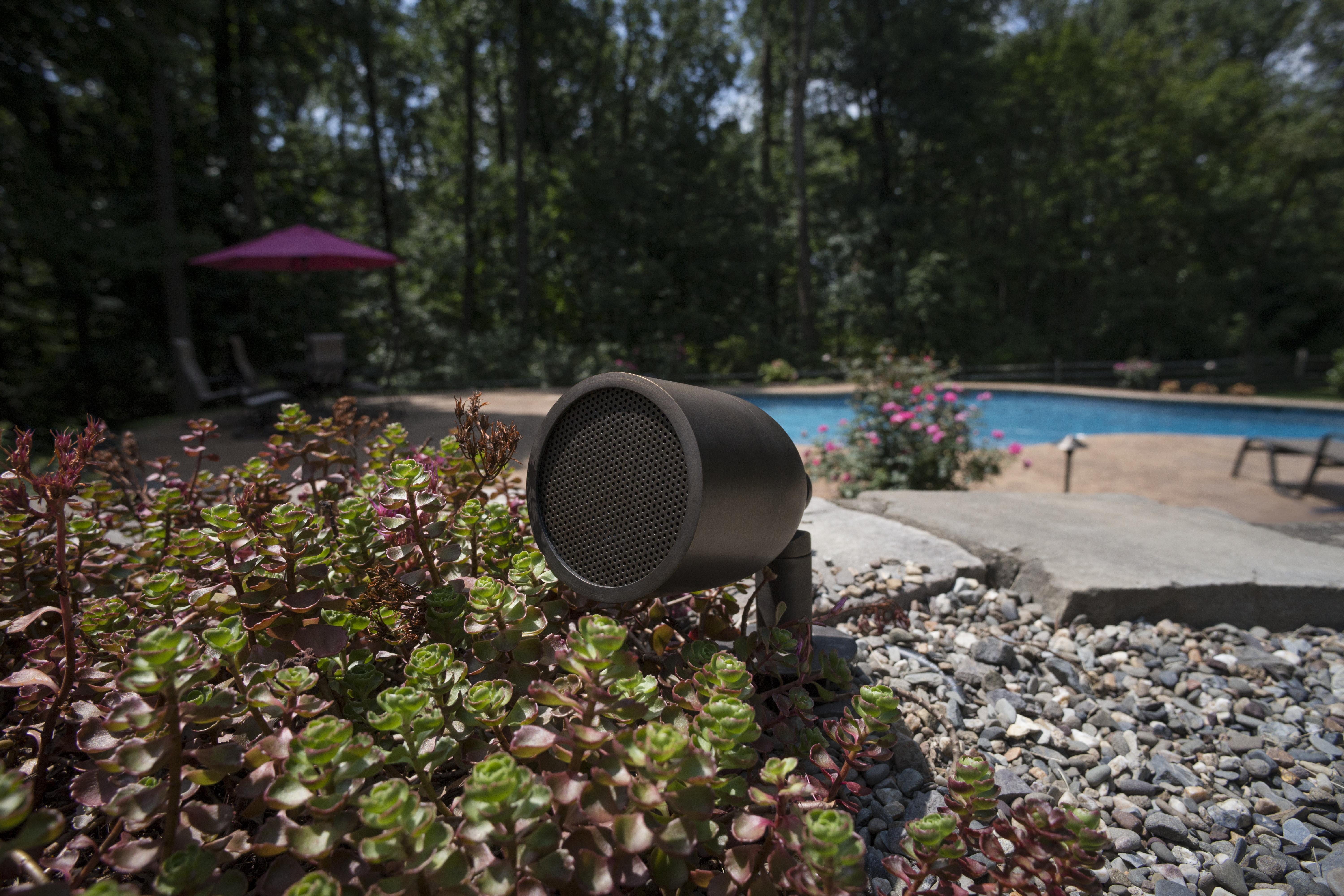 Closeup of a poolside speaker placed in a rockbed