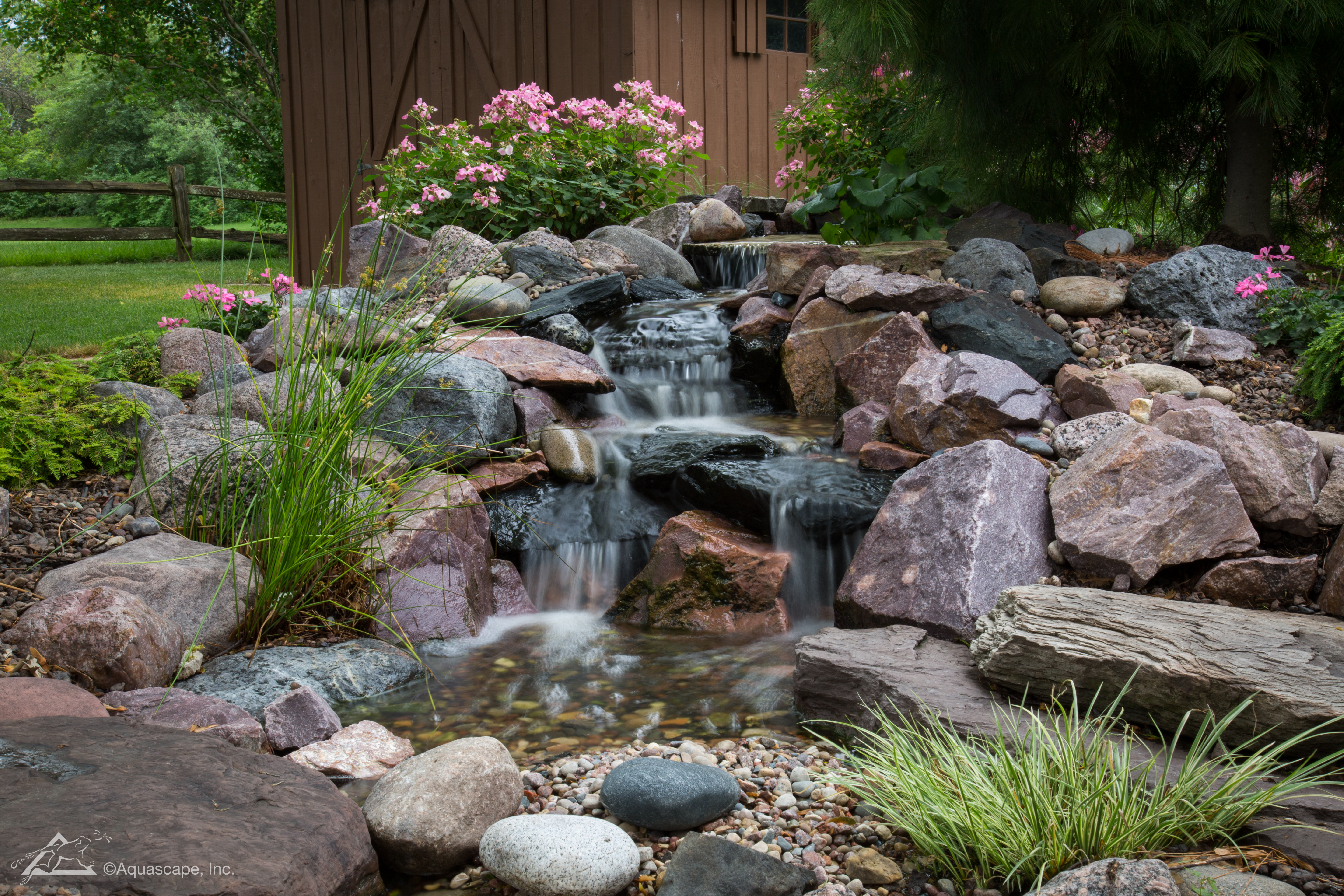 Small pondless waterfall water feature surrounded by rocks and plants
