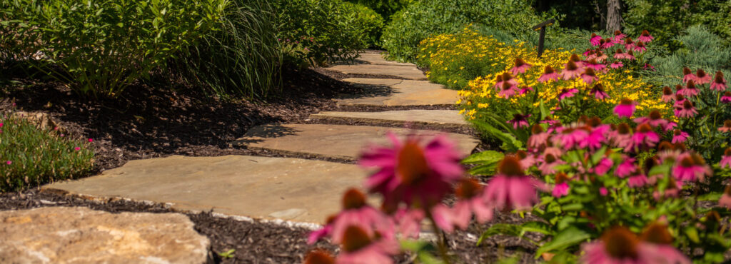 A well-maintained residential landscape featuring plants and a stone walkway.